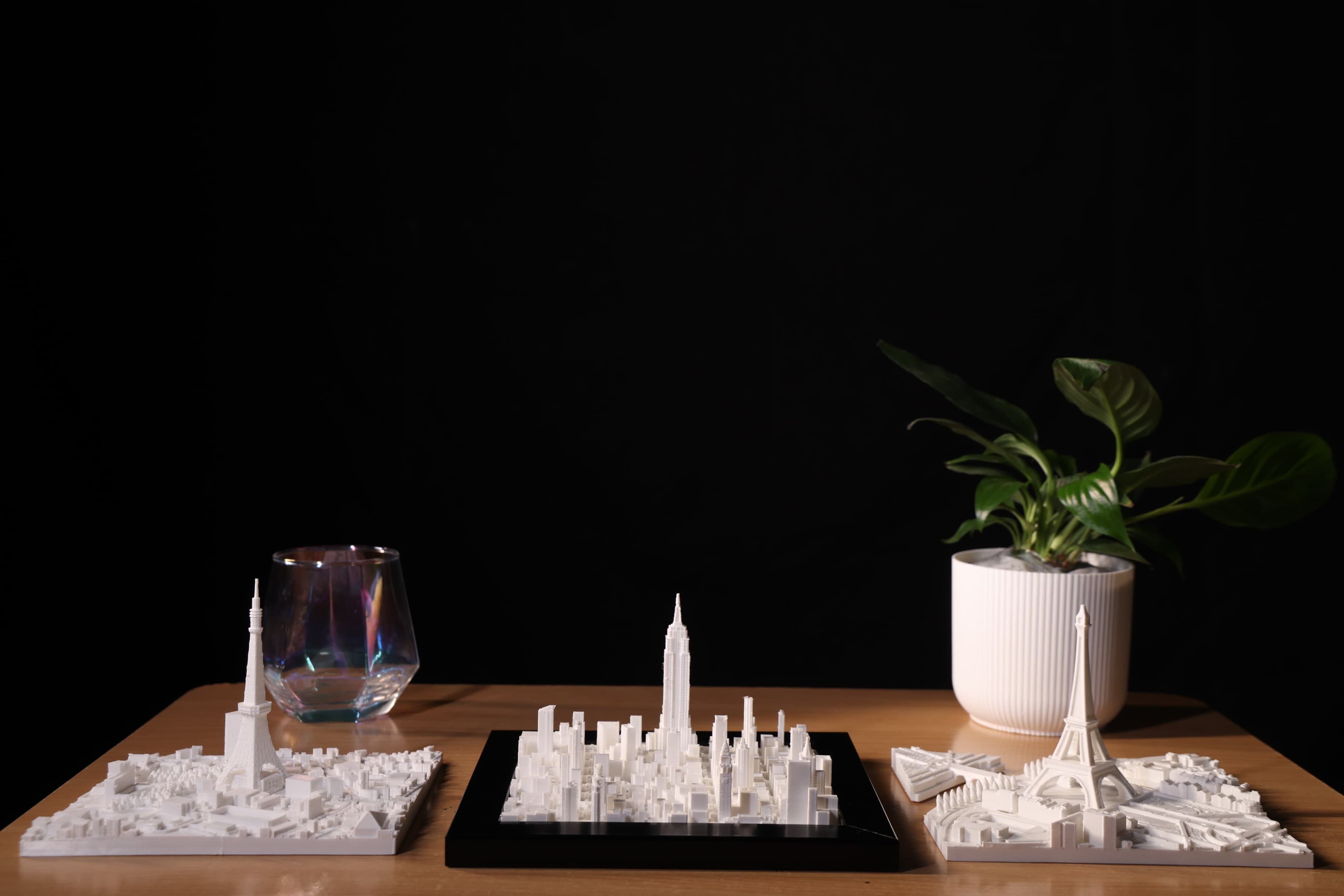 A white 3D-printed city skyline model in a black frame on a wooden desk